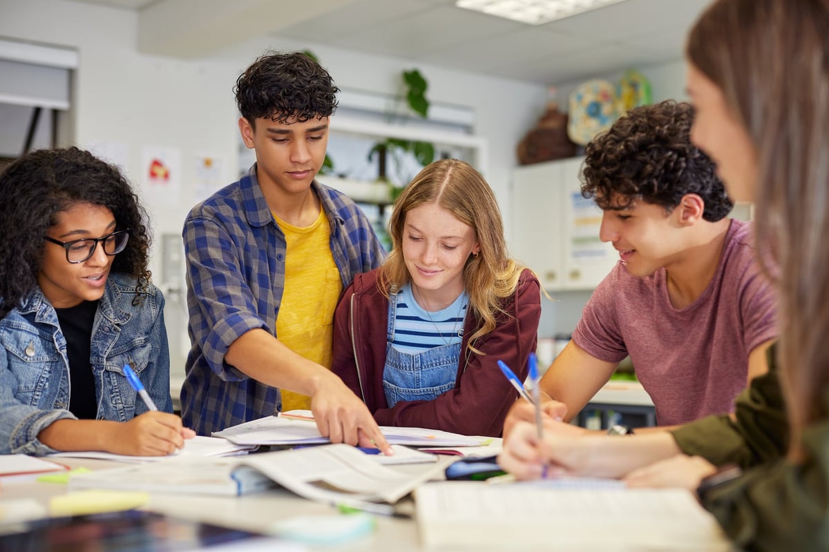 Diverse teenagers students group collaborating during a study session in classroom. Focused high school study group working together with books and notes while preparing for assignment.