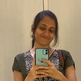 Woman taking a selfie in a mirror wearing an olive green shirt with patterned collar, holding a phone with light green case